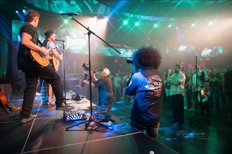 A guitarist performing beside the crowd under turquoise stage lights.